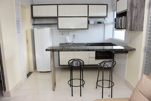 A compact kitchen with a built-in island, two bar stools, a refrigerator, and a microwave.