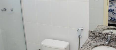 A bathroom with a glass shower enclosure, a white toilet, and a granite countertop sink.