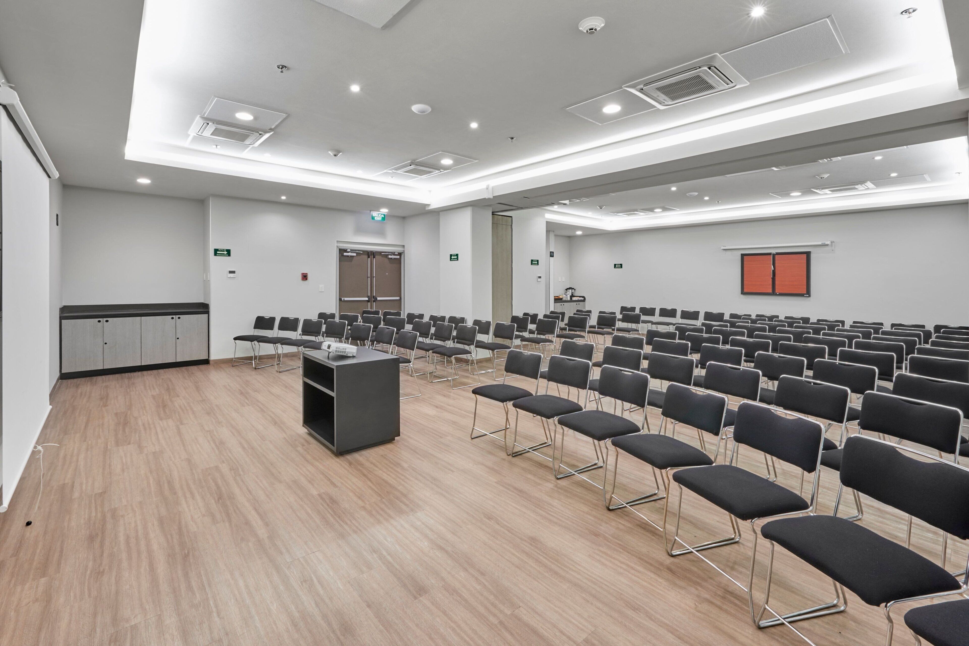 Un salón de conferencias con filas de sillas, un atril y una kitchenette.