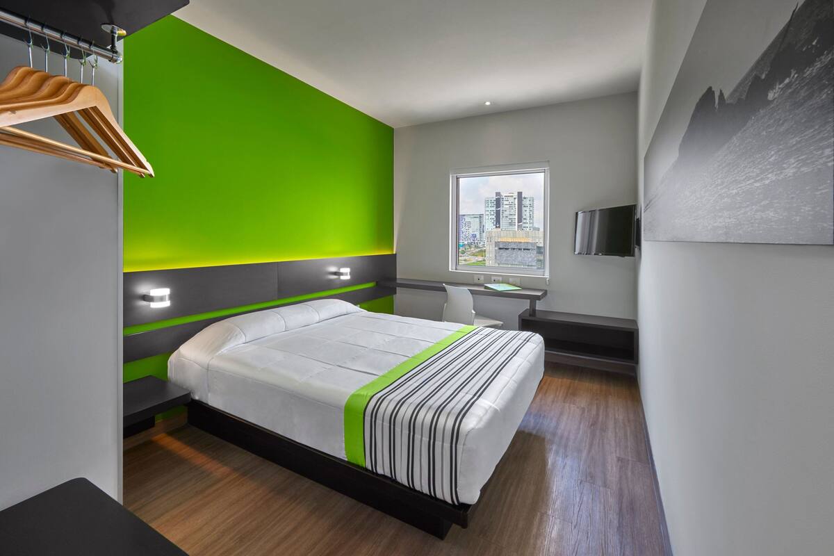A modern hotel room with a bed, a desk, and a window with a city view.