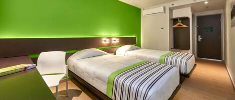 Habitación de hotel con dos camas, un escritorio y una silla. La pared es verde y hay una puerta con un perchero.