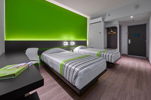 Een moderne hotelkamer met twee bedden, een bureau en een groene accentmuur.
