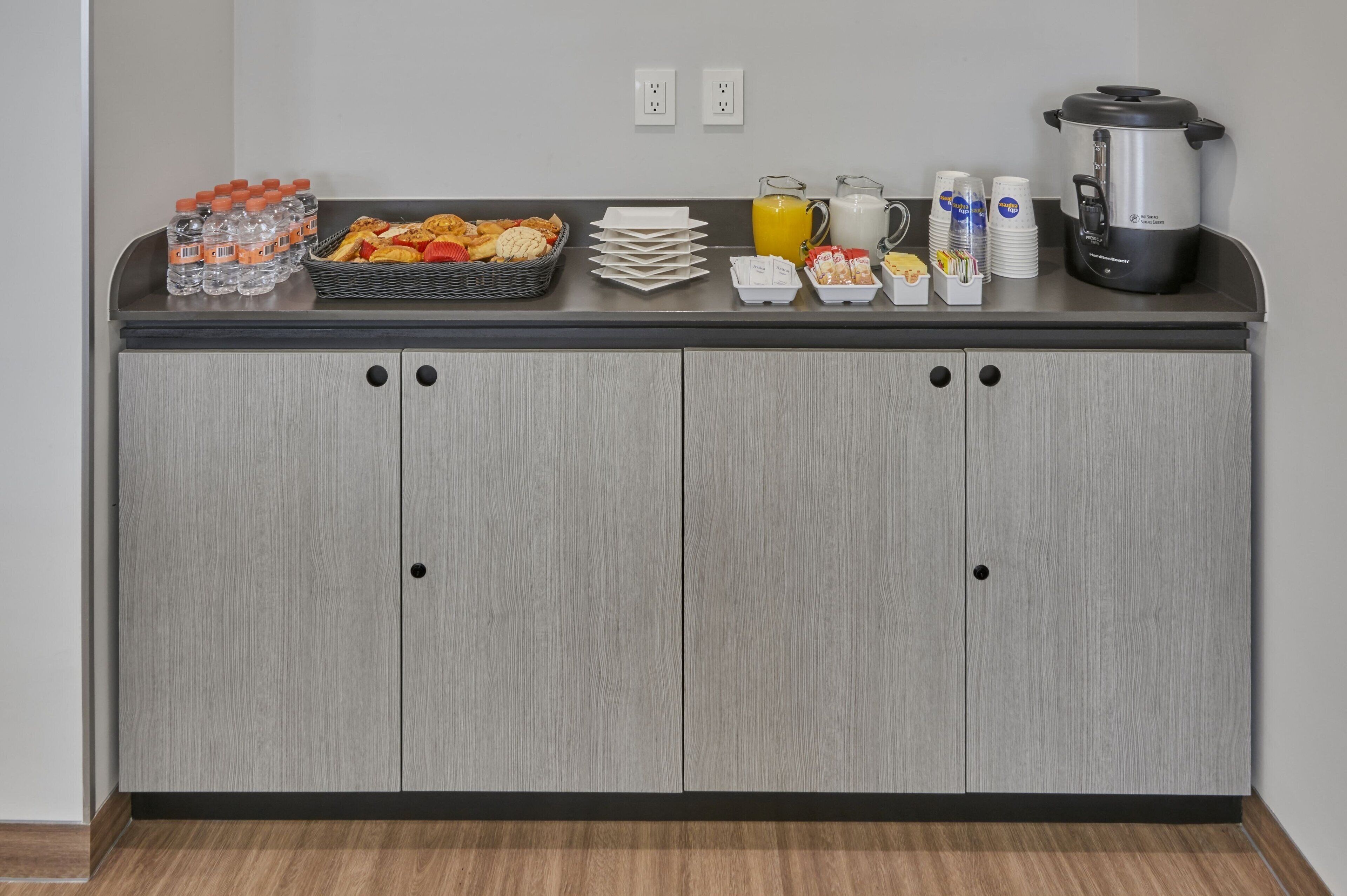 A kitchenette with a countertop, water bottles, a fruit basket, a coffee maker, and a slow cooker.
