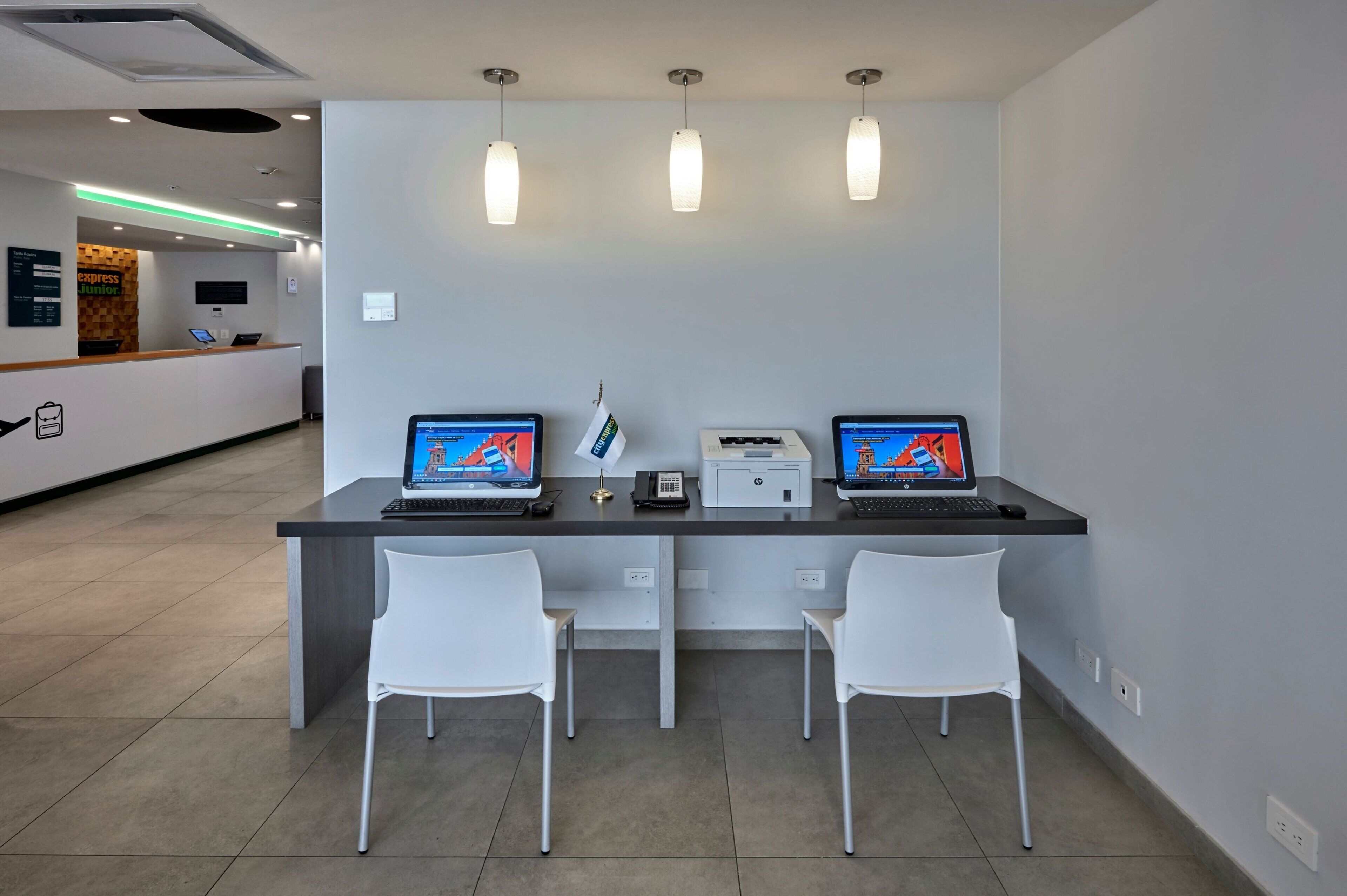 Een receptiebalie met twee laptops, een telefoon en een printer. Voor de balie staan twee witte stoelen.