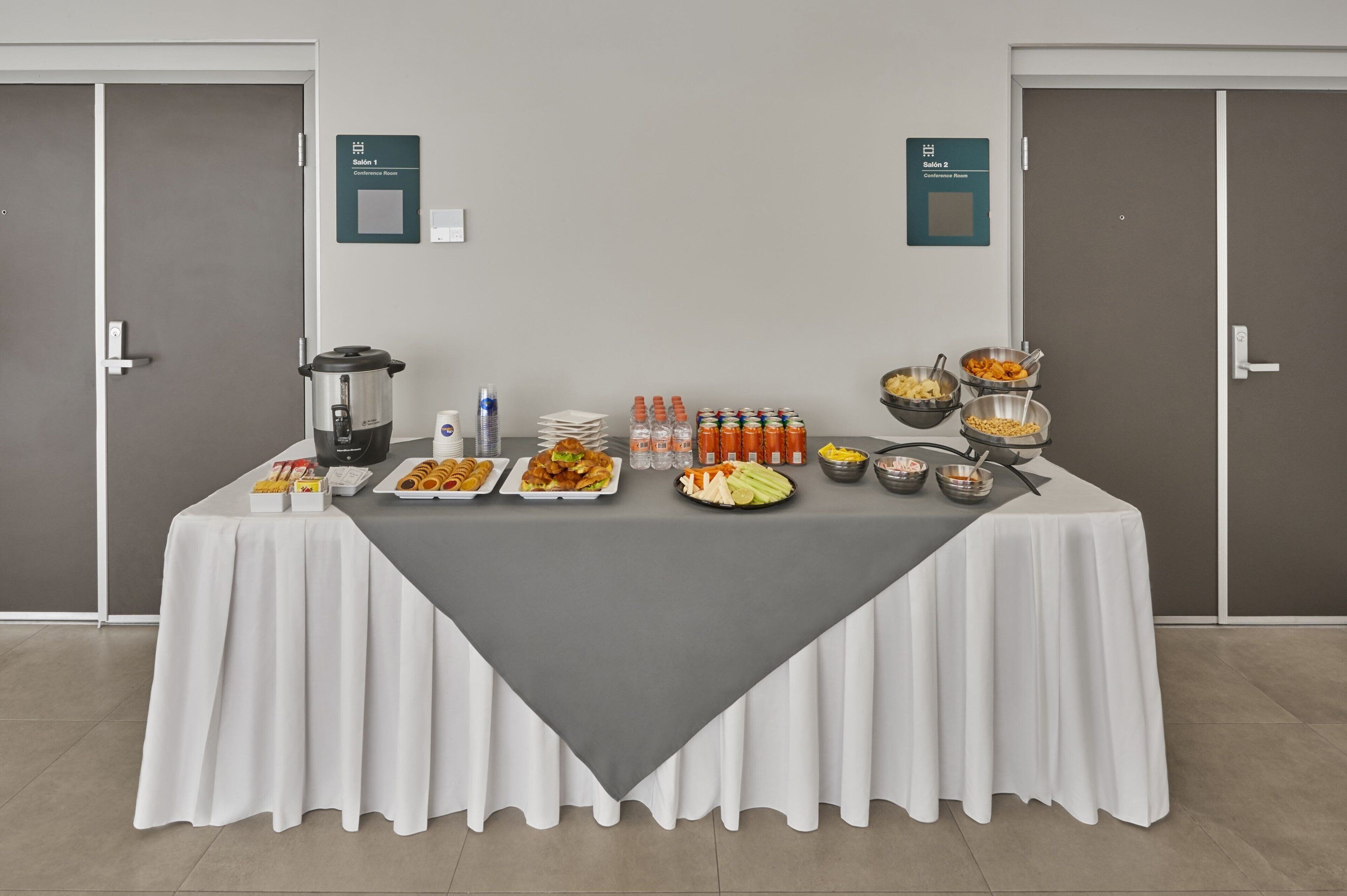 Ein reichhaltiges Buffet mit verschiedenen Speisen und Getränken, platziert in einem Raum mit zwei Türen und Hinweisschildern für Konferenzräume.