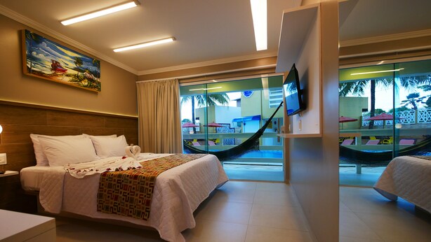 A hotel room with a bed, a TV, a hammock, and a view of the pool area. - Pousada Recanto dos Corais (Ipojuca)
