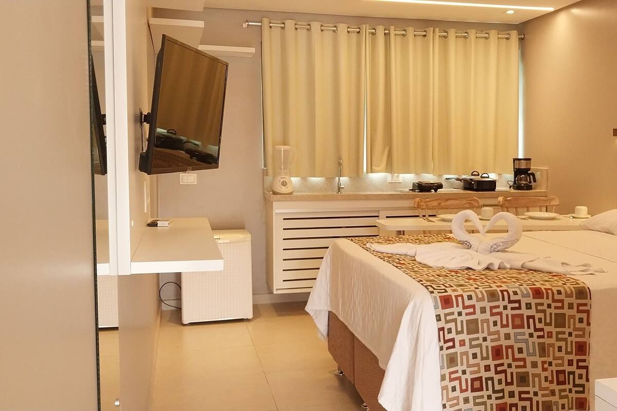 Hotellihuone, jossa on sänky, työpöytä, tuoli, televisio, kahvinkeitin ja ikkuna, jossa on verhot.