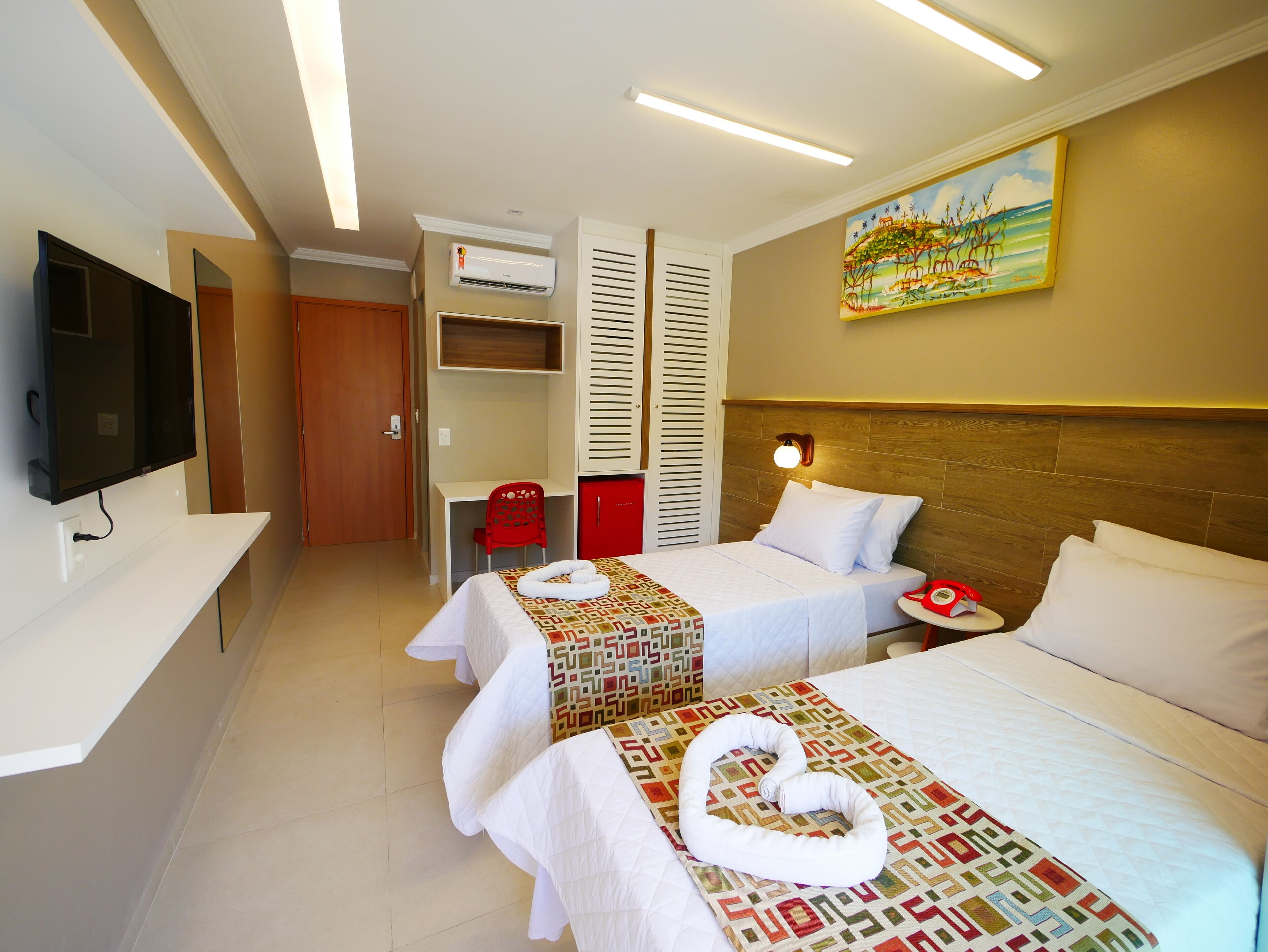 Habitación de hotel con dos camas, un televisor, un escritorio y un cuadro en la pared.