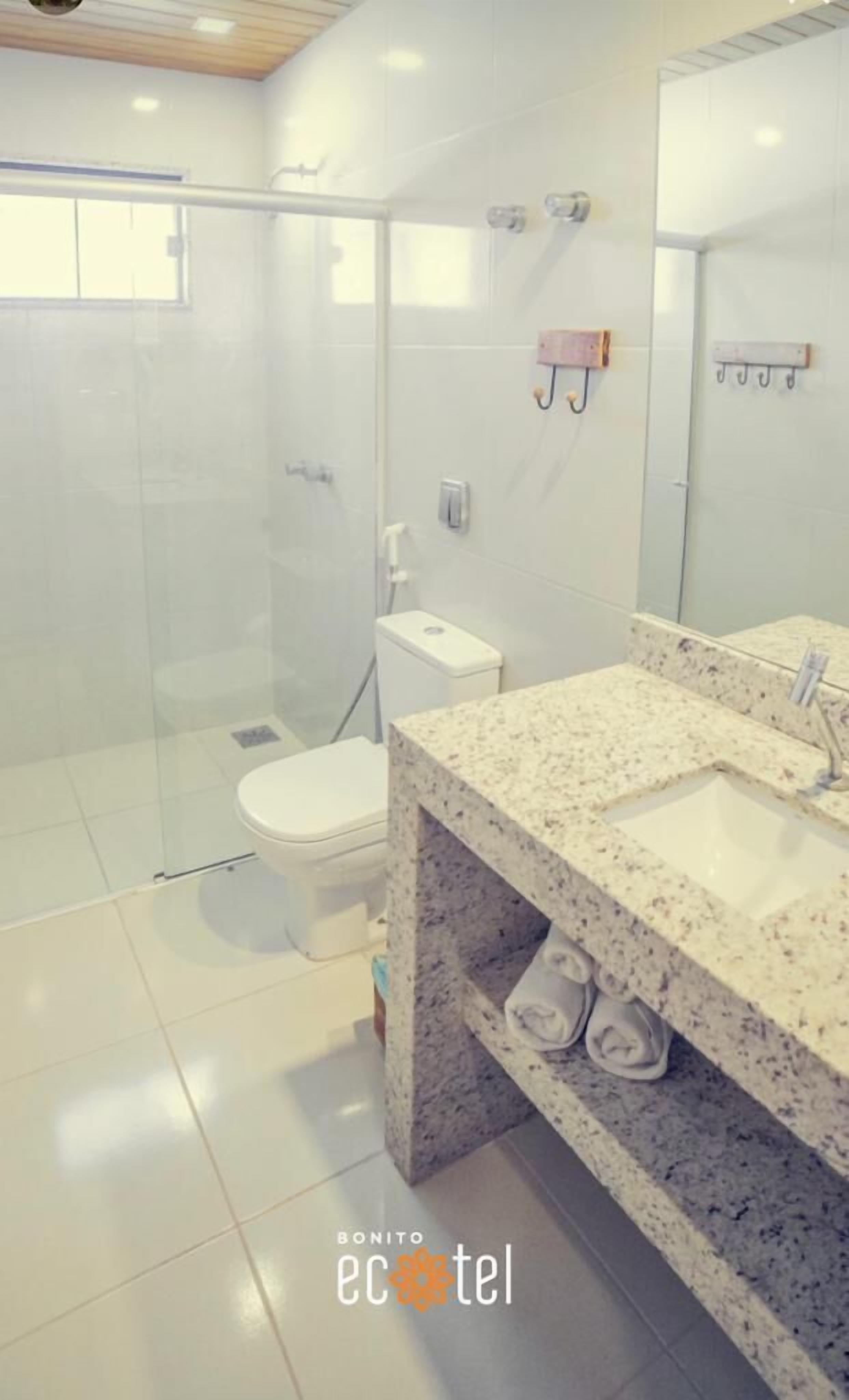 Une salle de bain moderne avec une douche à parois de verre, des toilettes blanches et un comptoir en granit avec un lavabo.