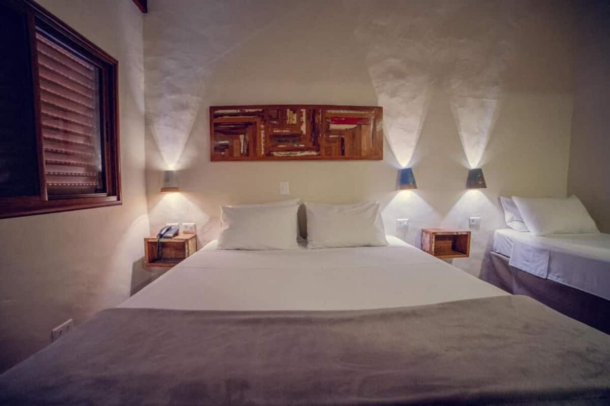 A hotel room with a large bed, two bedside tables, a wall-mounted artwork, and two wall-mounted lamps.