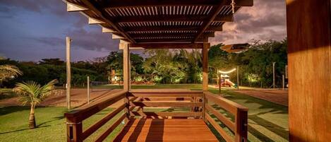 A wooden deck with a pergola overhead, surrounded by a well-maintained lawn and trees.