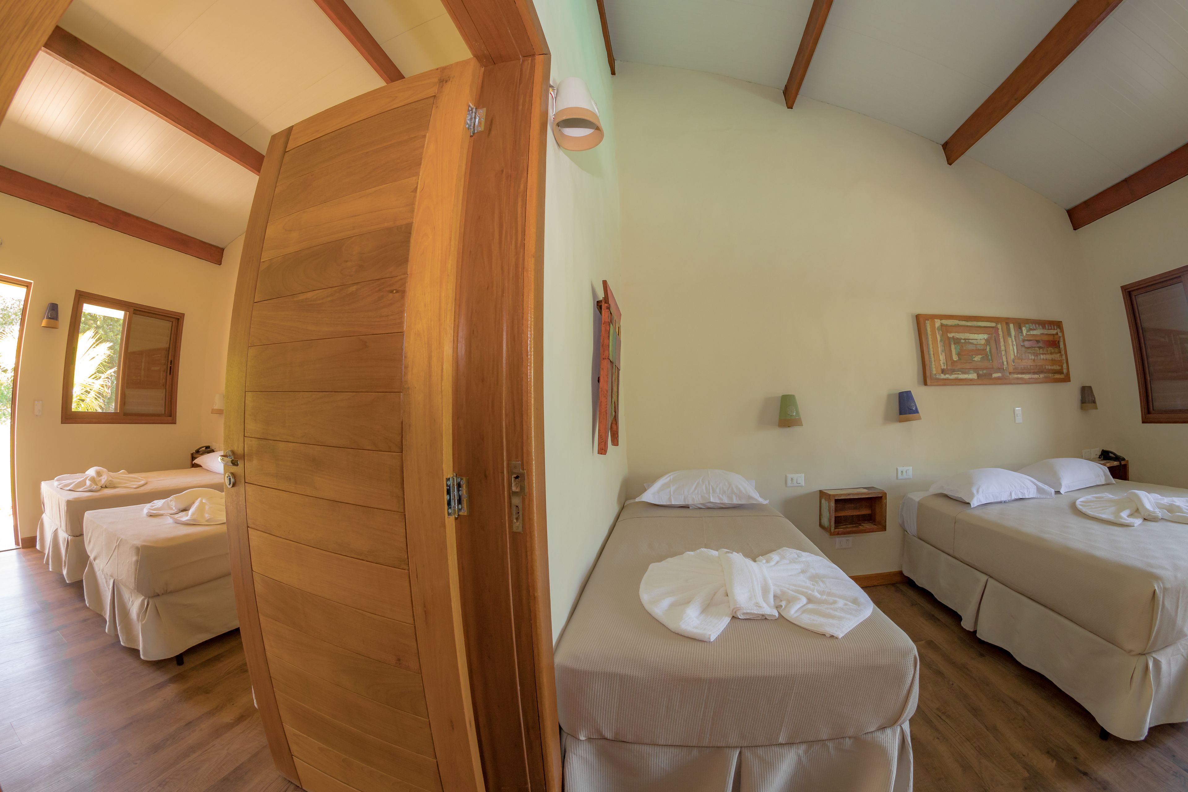 A room with wooden beams, three beds, a wooden door, and a small bedside table with a lamp.