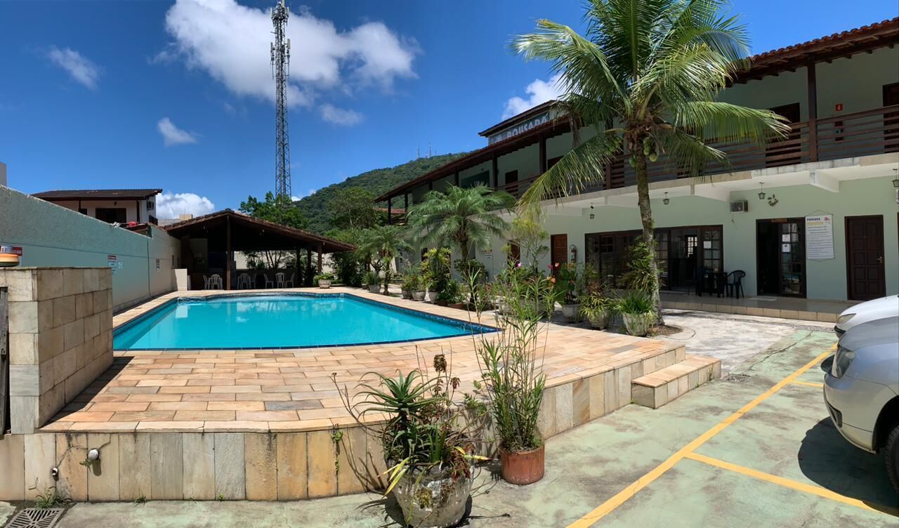 Piscina rodeada por plantas em vasos e um carro branco estacionado perto.