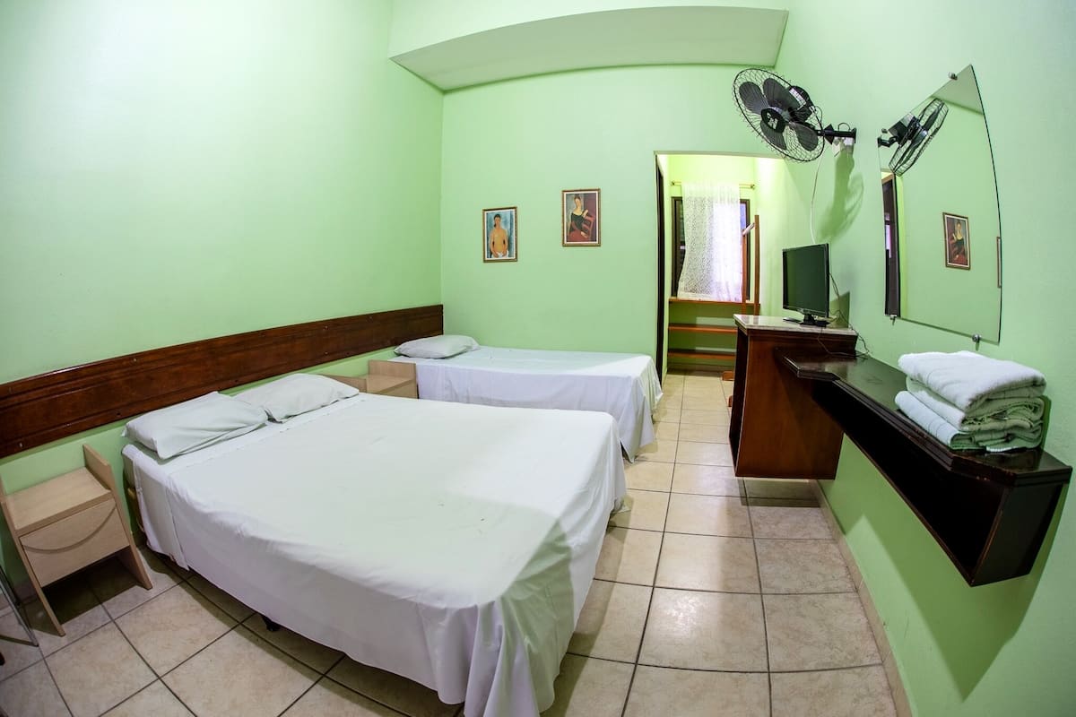 A hotel room with two beds, a desk, a mirror, and a TV.