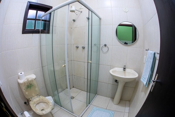 A bathroom with a glass-enclosed shower, a toilet, a sink, and a mirror. - Pousada Marwille (Guarujá)
