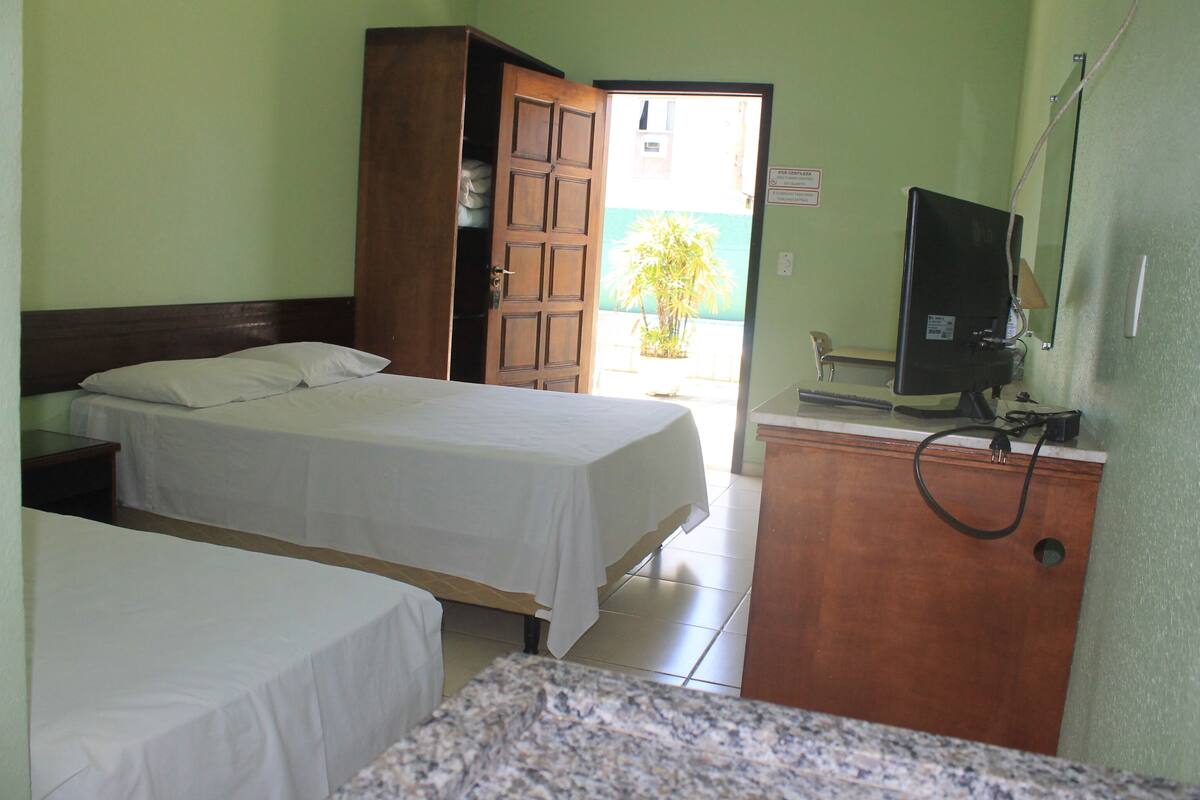 A hotel room with two beds, a wooden wardrobe, a television, and a view of the outside.