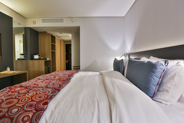 Habitación de hotel con cama, escritorio con cafetera y espejo.