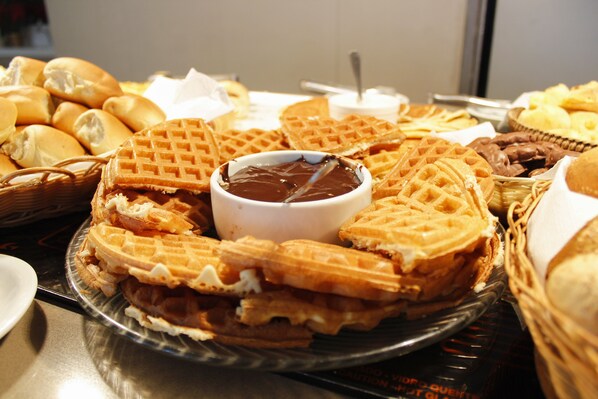 A variety of waffles and pastries on a tray, including a bowl of chocolate sauce. - Hilton Garden Inn Santo André (Santo André)