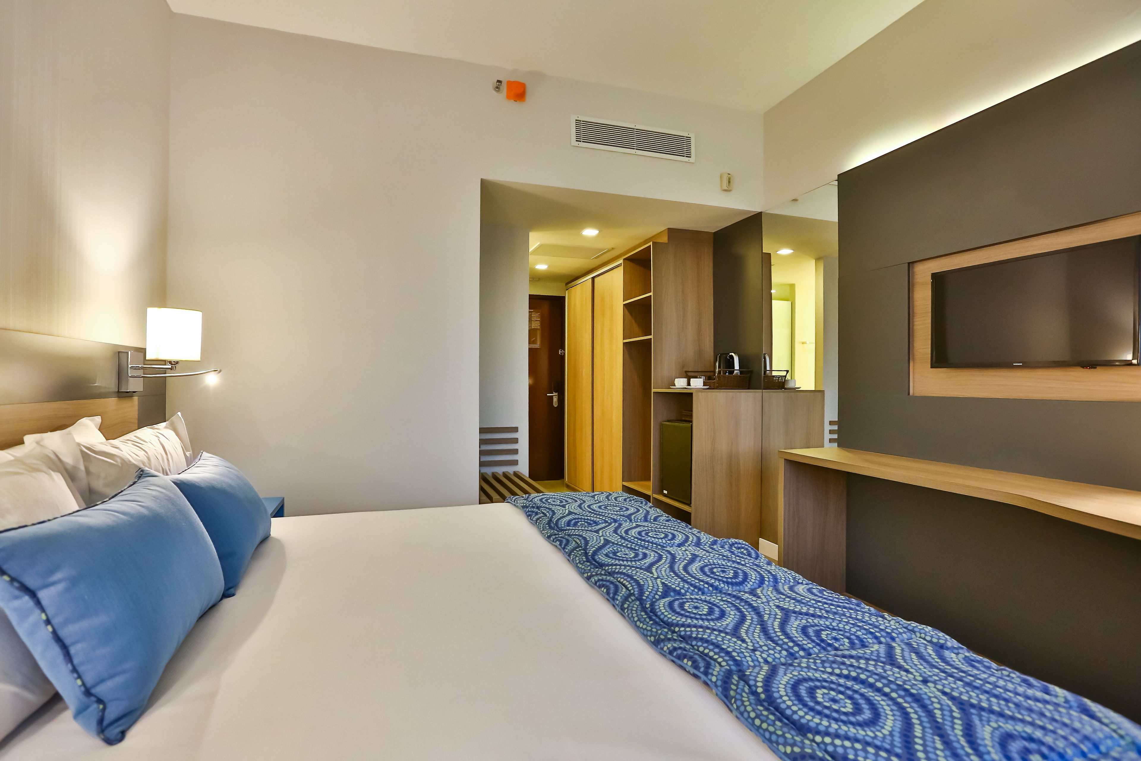 Una habitación de hotel con cama, televisor montado en la pared y armario.