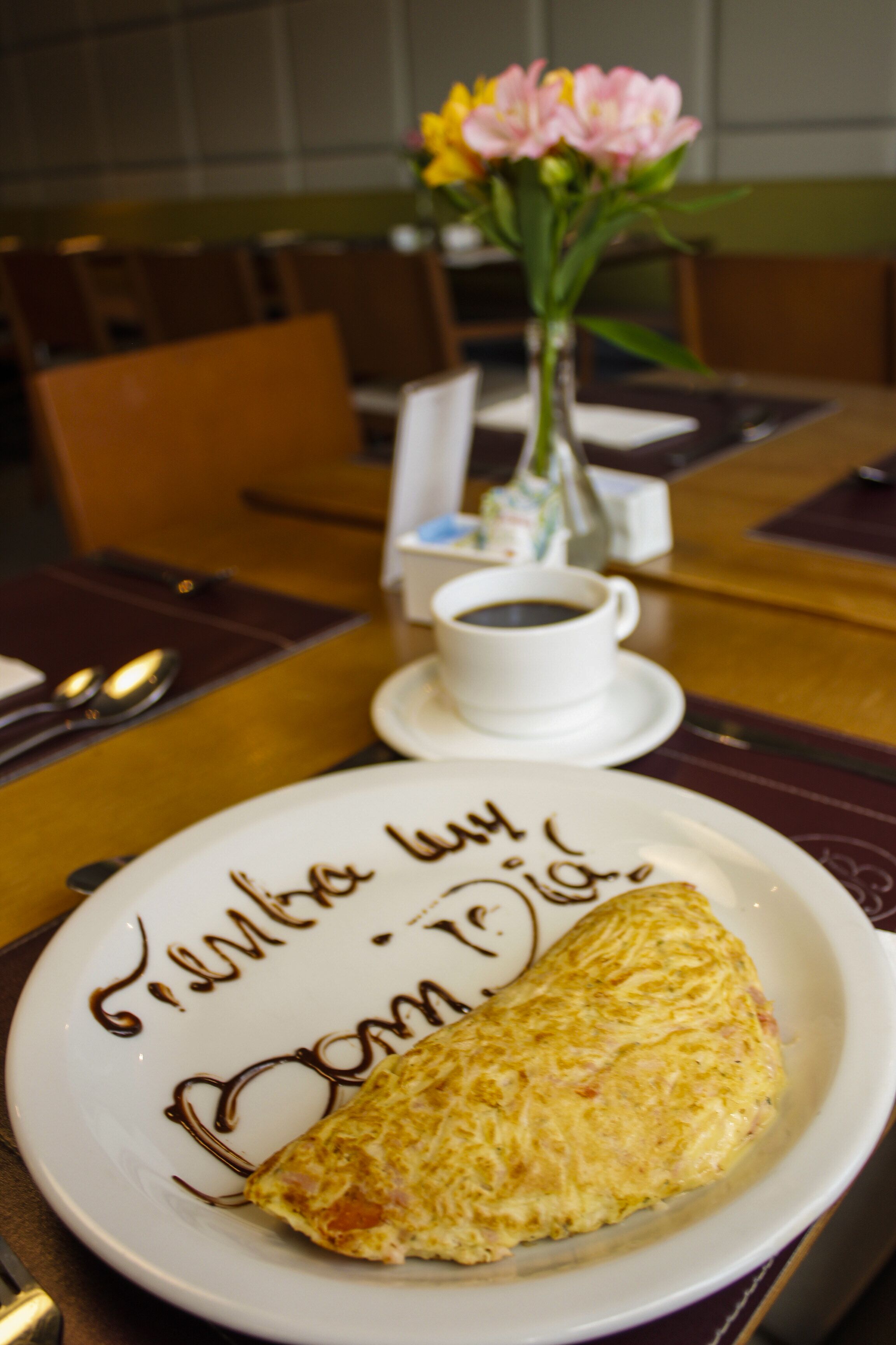 A plate with an omelette and a cup of coffee on a table with a vase of flowers in the background.