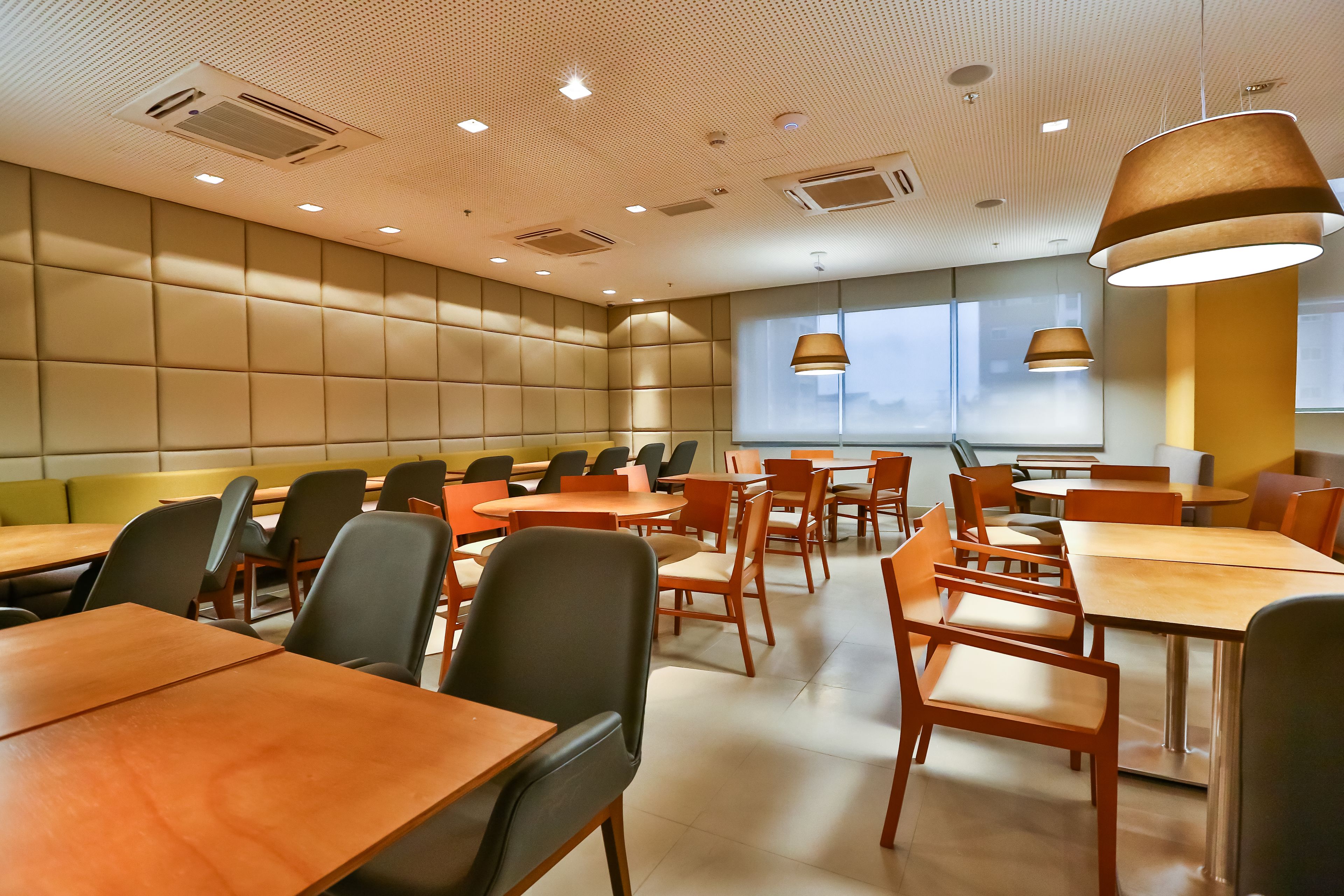 A modern dining area with multiple tables and chairs, recessed ceiling lighting, and large windows.