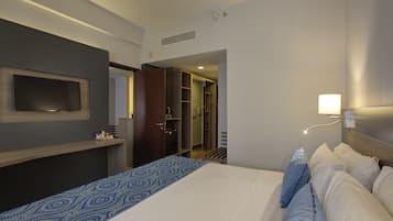 A hotel room with a bed, a TV mounted on the wall, a bedside table, and a walk-in closet.