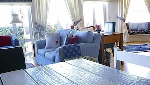 A dining table with a plate of fruit in a room with a sofa, a fan, and curtains. - Harbour Place (Cape Town)