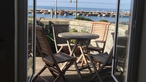 A view from a room with a large window overlooking a harbor, featuring a wooden deck with a round table and chairs. - Harbour Place (Cape Town)