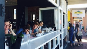 An outdoor dining area with a long white counter, multiple stools, and a brick-paved walkway. - Harbour Place (Cape Town)