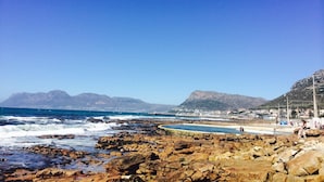 A rocky beach with a clear view of the ocean and distant mountains. - Harbour Place (Cape Town)