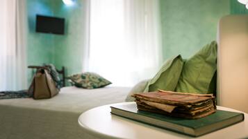 A hotel room with a bed, a bedside table with a book, a lamp, and a television on the wall.