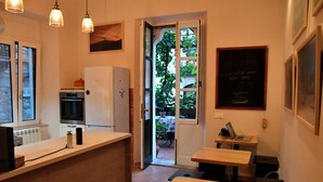 Cocina compacta con refrigerador, horno y microondas. Hay mesas de madera y un banco. Una puerta da al exterior.