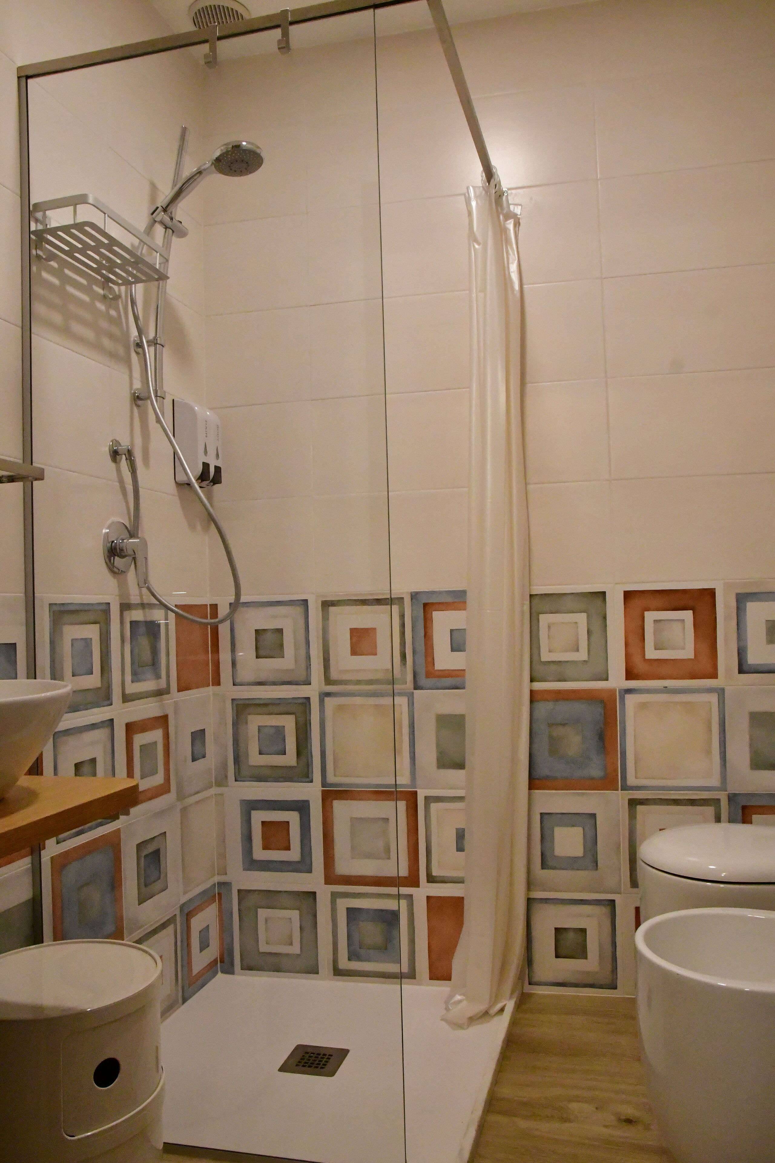 A bathroom with a shower, toilet, sink, and a patterned tile wall.