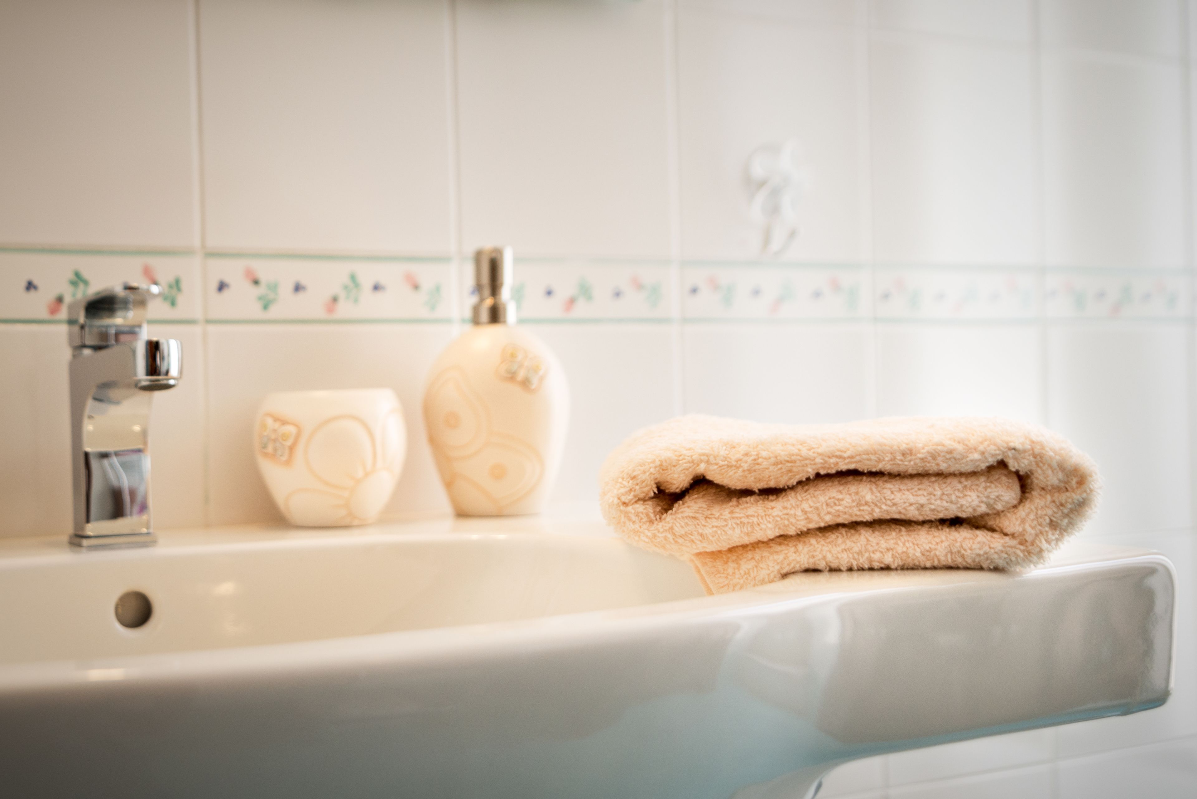 A bathroom with a white sink, a soap dispenser, and a folded towel on the edge.