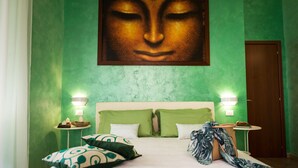 Habitación de hotel con pared verde, un cuadro grande sobre la cama, dos mesitas de noche con lámparas y una puerta de madera.