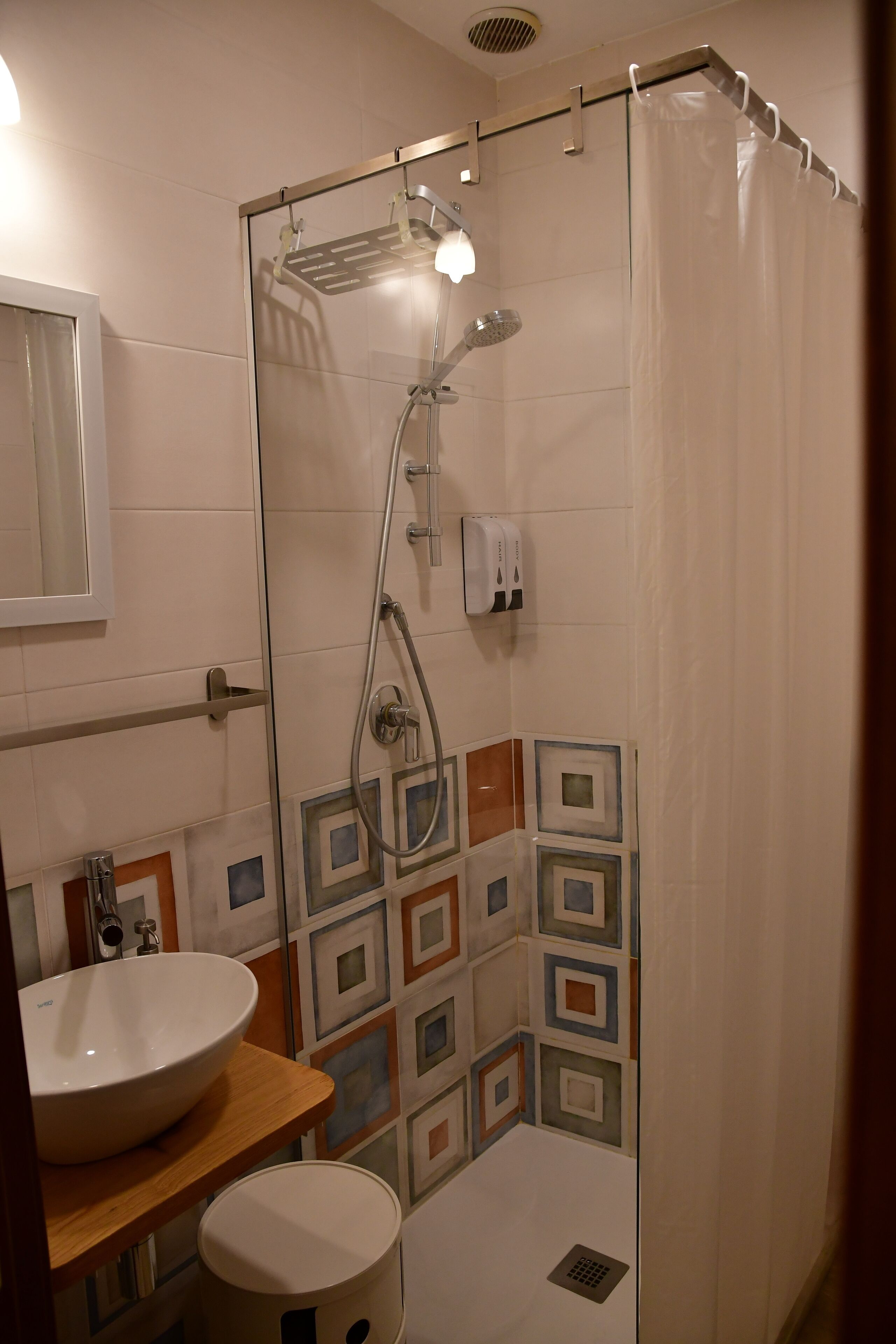 Un bagno con doccia vetrata, lavabo con piano in legno e parete rivestita in piastrelle con motivo geometrico.