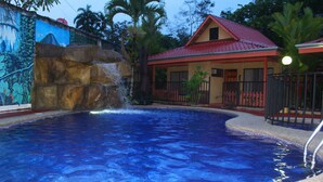 Una piscina con cascata, circondata da una recinzione e palme.