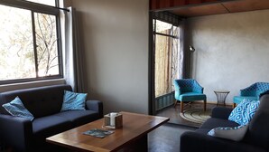 Una sala de estar con un sofá oscuro, una mesa de centro de madera y dos sillones azules.