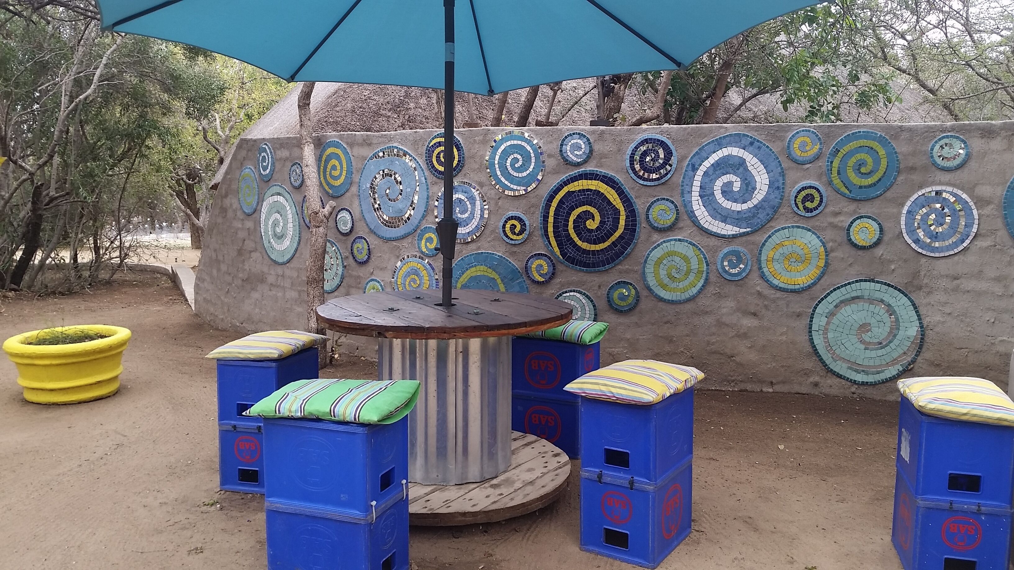 A seating area with a round table, blue plastic stools, and a colorful mosaic wall.
