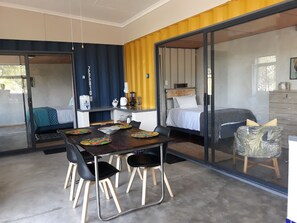A modern room with a dining table, two beds, and a kitchen area. - 24 Degrees Self-Catering (Hoedspruit)