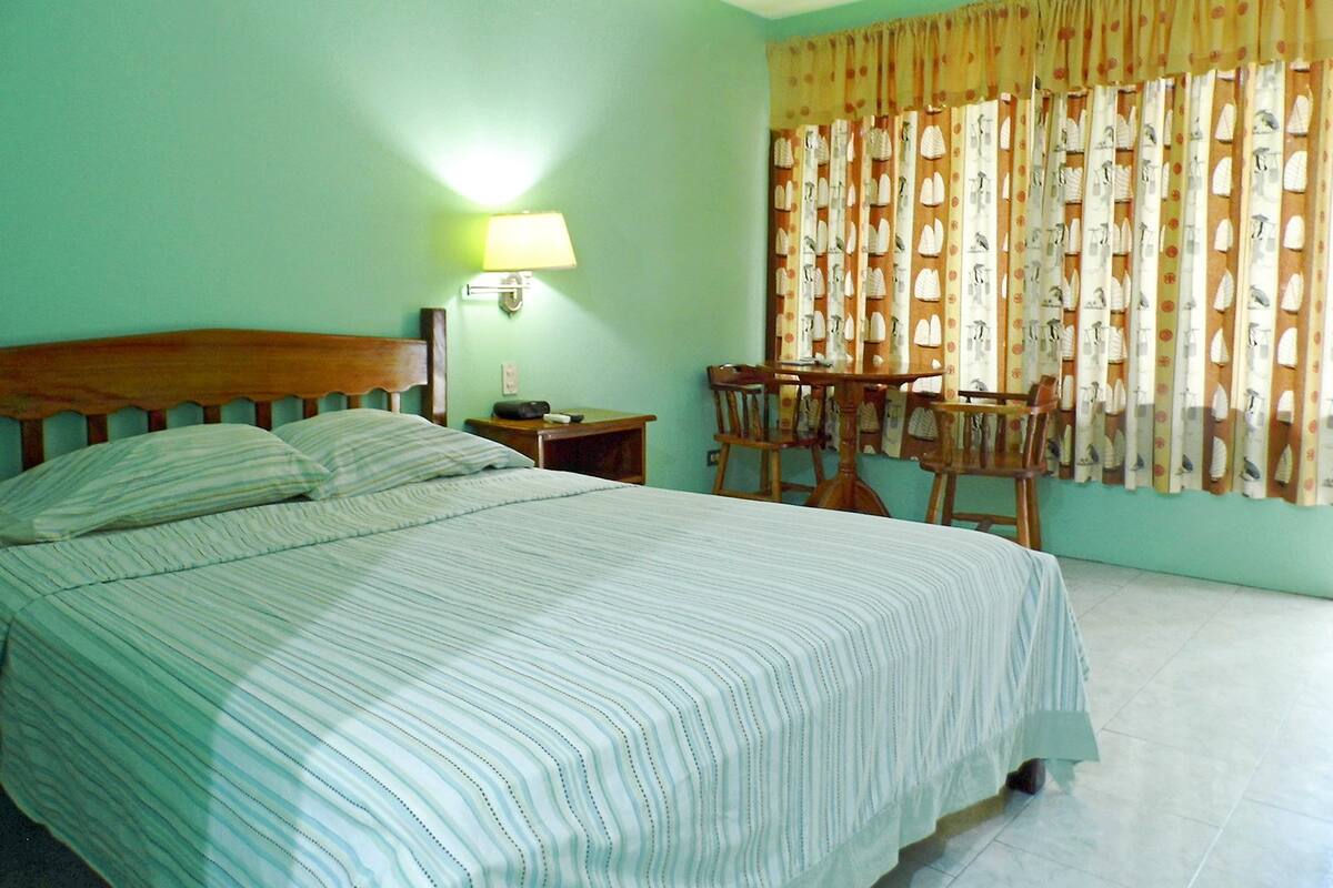 A hotel room with a bed, a nightstand, a table with chairs, and a window with curtains.