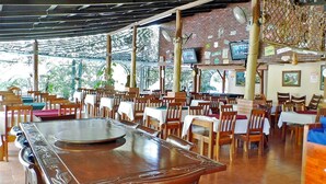A restaurant with wooden tables and chairs, a large central table, and a brick wall with various decorations. - Hotel Río Tempisque (Nicoya)