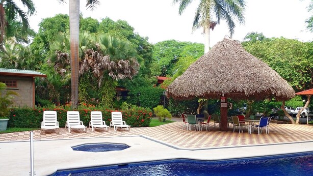 A swimming pool with a thatched-roof gazebo, lounge chairs, and a dining area with tables and chairs. - Hotel Río Tempisque (Nicoya)