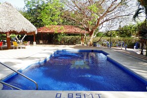 A swimming pool with a thatched roof structure and lounge chairs around it.