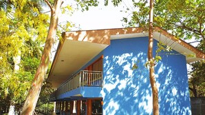 A two-story building with a blue facade, a balcony on the upper floor, and a covered walkway leading to the entrance. - Hotel Río Tempisque (Nicoya)