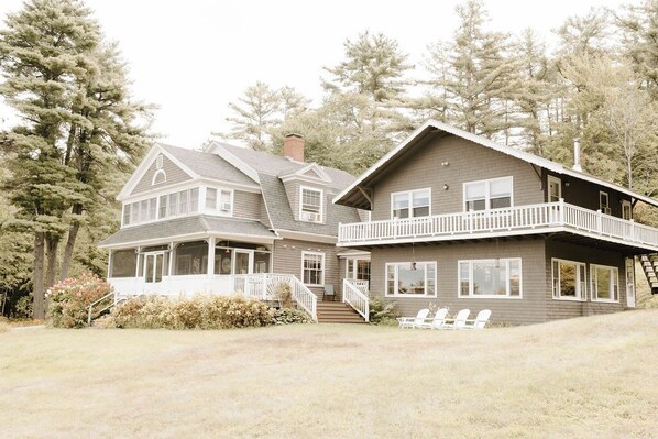Stunning two-story home with a central entrance and covered porch, set amidst a serene landscape of mature trees and a well-manicured lawn.