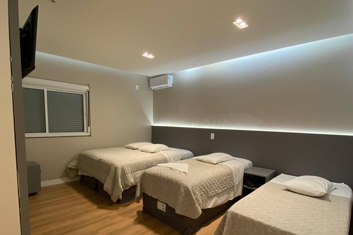 A modern bedroom with three single beds, a window, and an air conditioning unit.