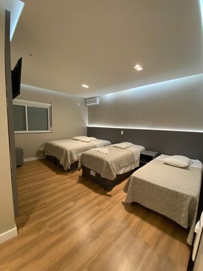 A modern bedroom with three single beds, a window, and an air conditioning unit. - North Hotel (Chapecó)