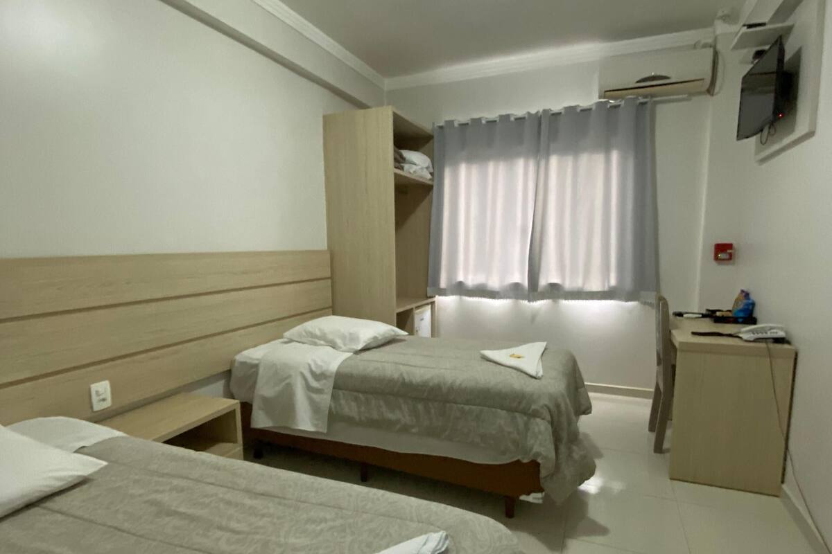 A hotel room with two beds, a desk, a chair, a wardrobe, and a TV mounted on the wall.