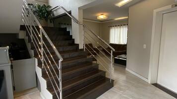 A modern staircase with metal railings, leading to a second floor. The floor is tiled, and there is a plant on the landing.